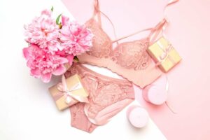 Ensemble lingerie avec soutien-gorge et culotte, accompagné de deux petits paquets cadeau et d'un bouquet de fleurs roses.