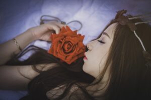 Femme avec une couronne de fleurs tenant une rose, allongée rêveusement.