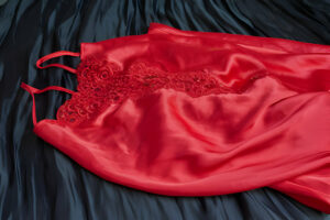Nuisette rouge satinée avec ornements en dentelle, délicatement disposée sur un drapé de satin noir.