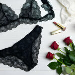 Ensemble de lingerie noire en dentelle avec des roses rouges, des perles et du maquillage sur un fond blanc.