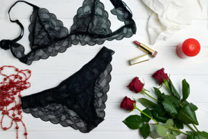 Ensemble de lingerie noire en dentelle avec des roses rouges, des perles et du maquillage sur un fond blanc.