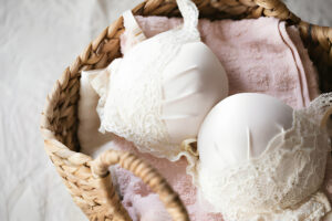 Panier en osier contenant de la lingerie féminine en dentelle blanche et une serviette rose.