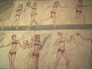 Mosaïque antique illustrant l’histoire du bikini, montrant des femmes en tenues ressemblant au bikini moderne.